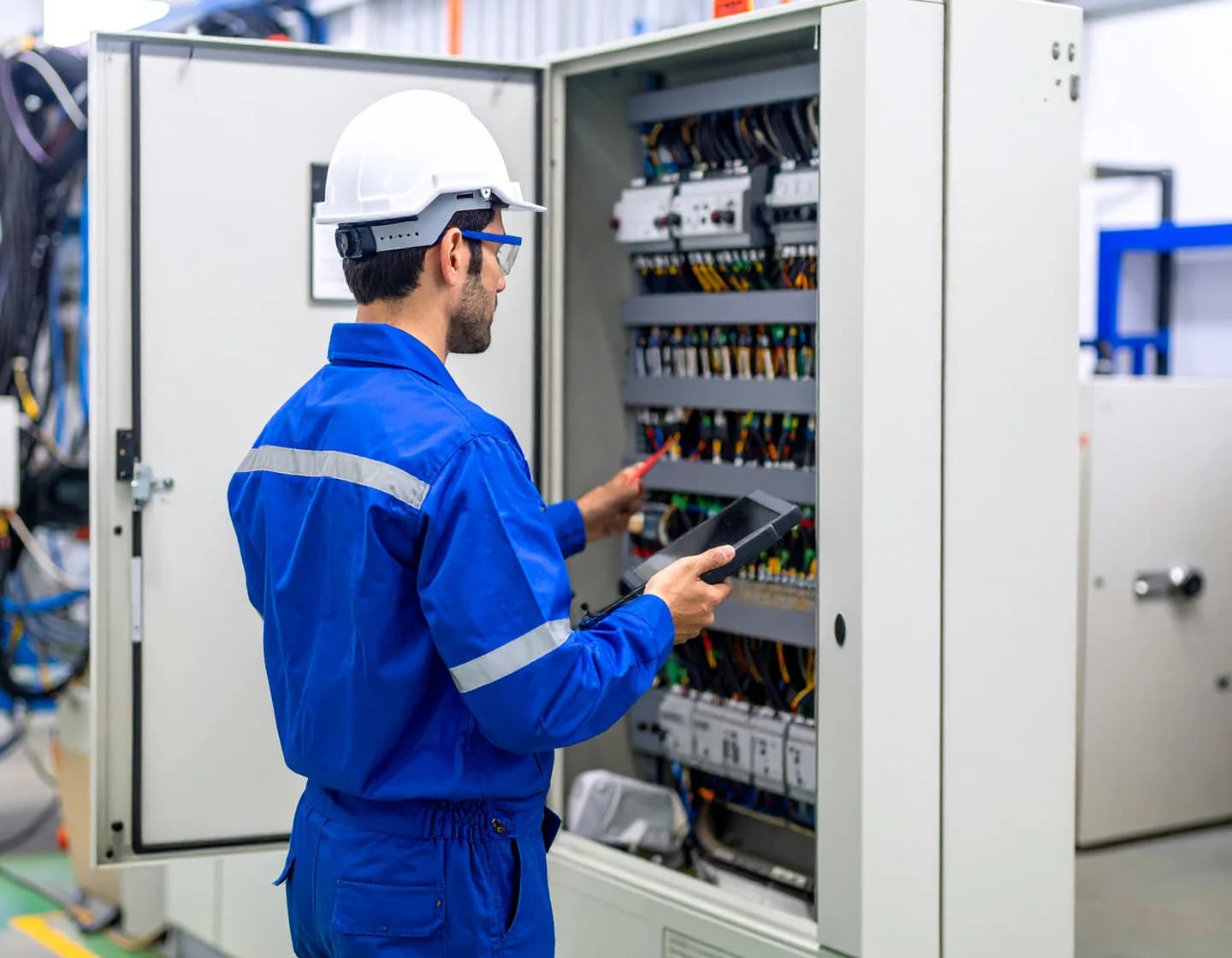 Elektrik panosunun önünde ölçüm cihazı tutan teknik çalışan