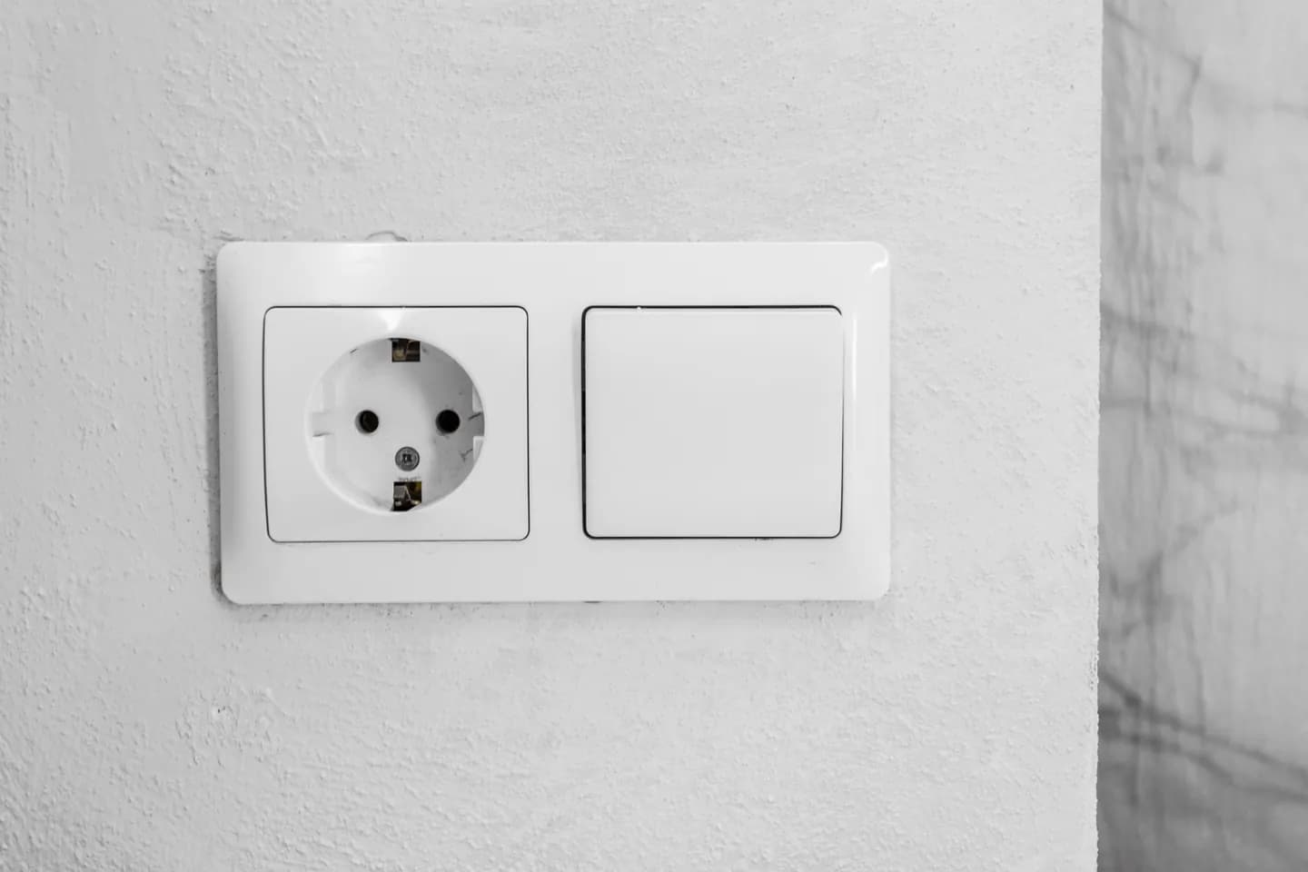 Beyaz duvarda yan yana topraklı priz ve elektrik anahtarı